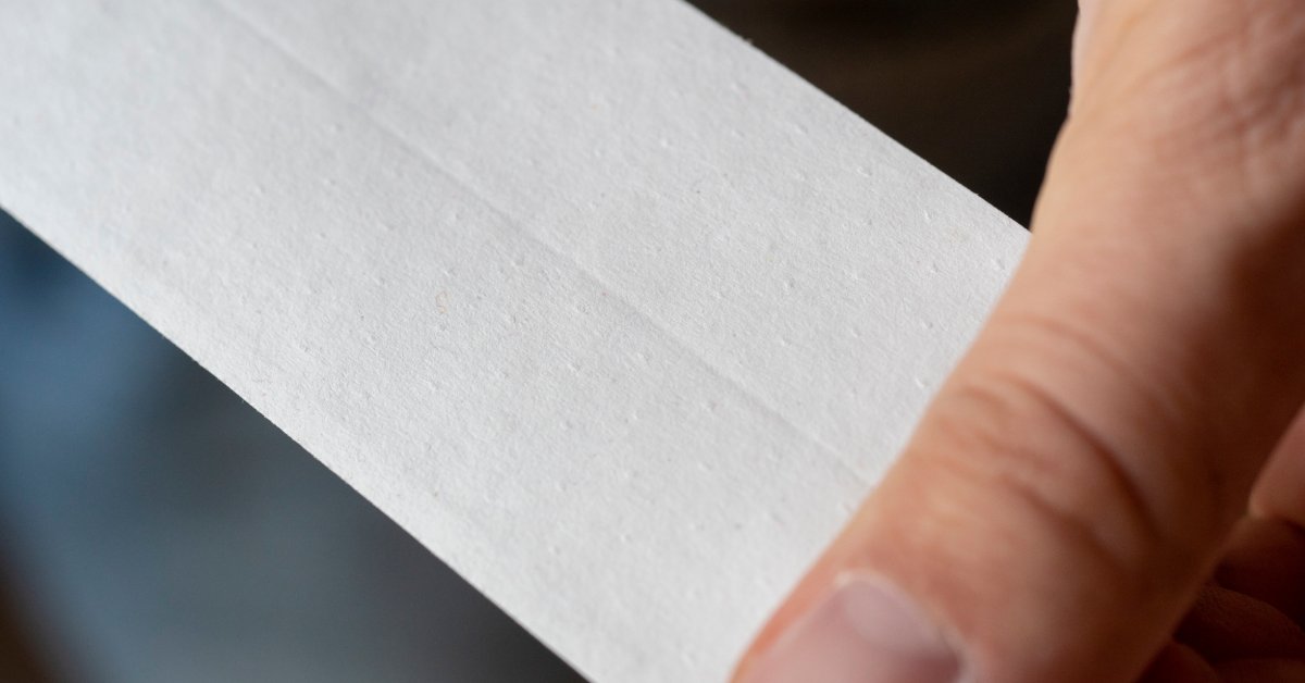 A close-up of perforated paper drywall tape with rows of small holes across a tan surface and a soft background.