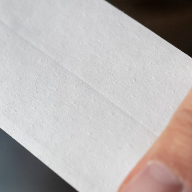 A close-up of perforated paper drywall tape with rows of small holes across a tan surface and a soft background.