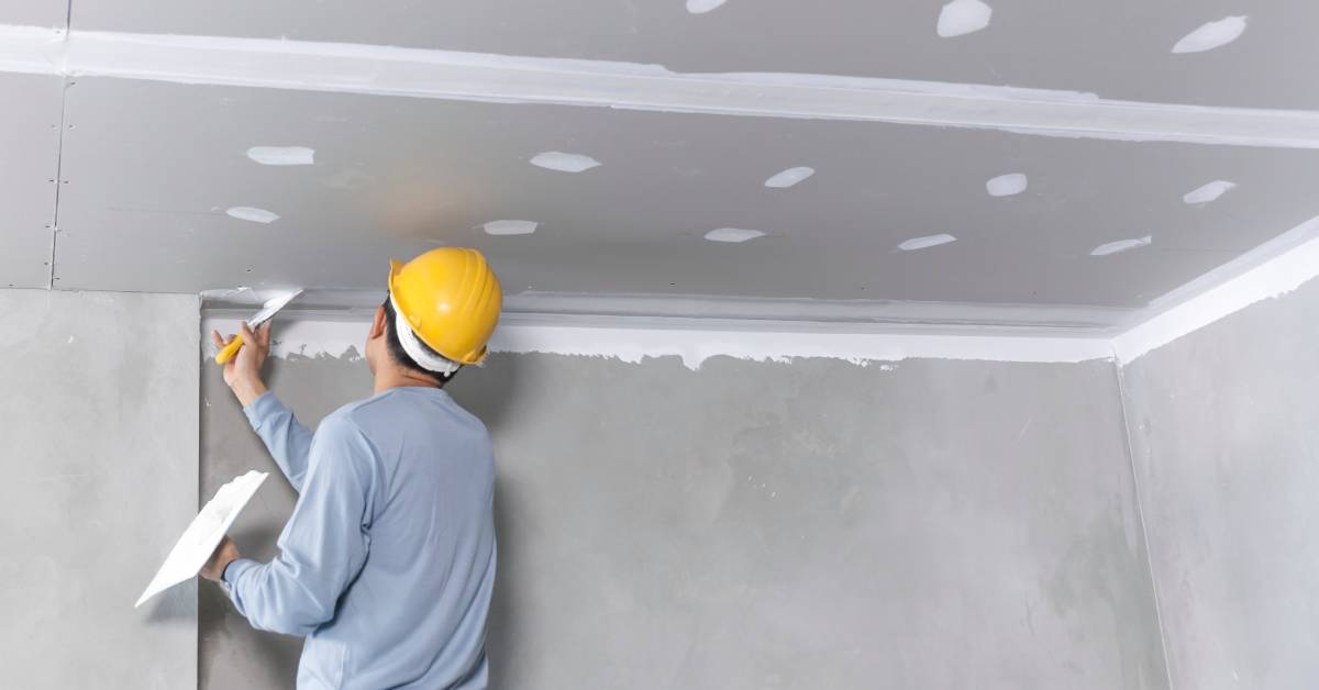 A craftsman working on a plaster gypsum ceiling, carefully installing and smoothing gypsum board for a clean finish.