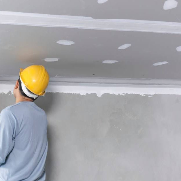 A craftsman working on a plaster gypsum ceiling, carefully installing and smoothing gypsum board for a clean finish.