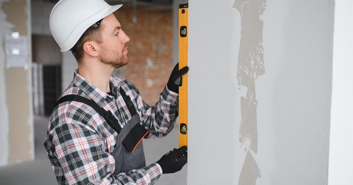 A man holding a spirit level against a wall during interior renovation work while wearing safety gear.