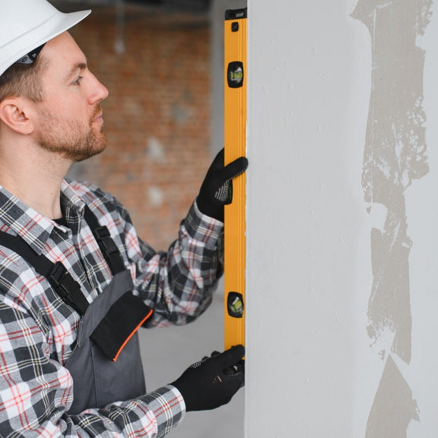 A man holding a spirit level against a wall during interior renovation work while wearing safety gear.